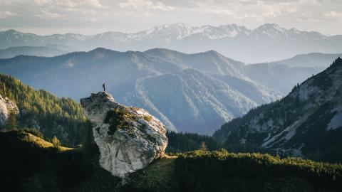 Person standing on boulder facing mountain range